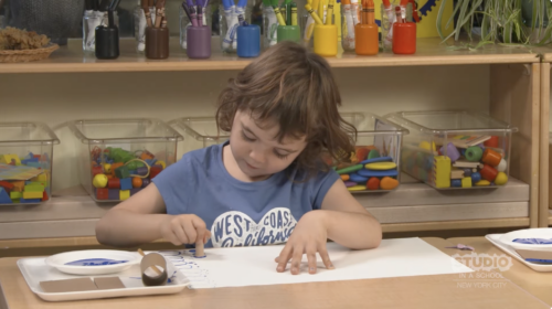 child stamping with blue paint on a white sheet of paper
