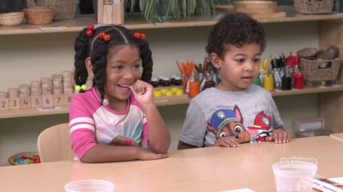 2 children sitting at a shared desk with water cups infront