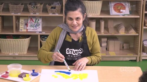 teacher with blue and yellow paint on a white paper in front